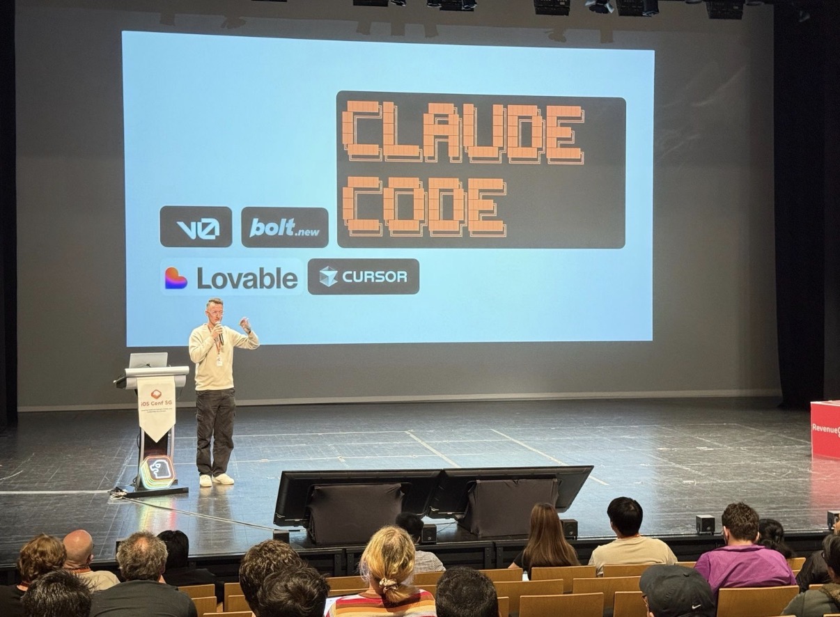 Fiachra MacFadden on stage at iOS Conf SG in Singapore, in front of a large slide listing the tools he used to build his app. The audience is seated in front of the stage.