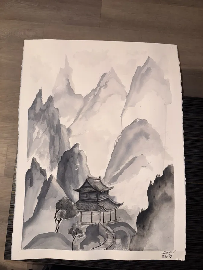 An ink wash painting of a pagoda among misty mountain peaks, unframed on a wooden floor.