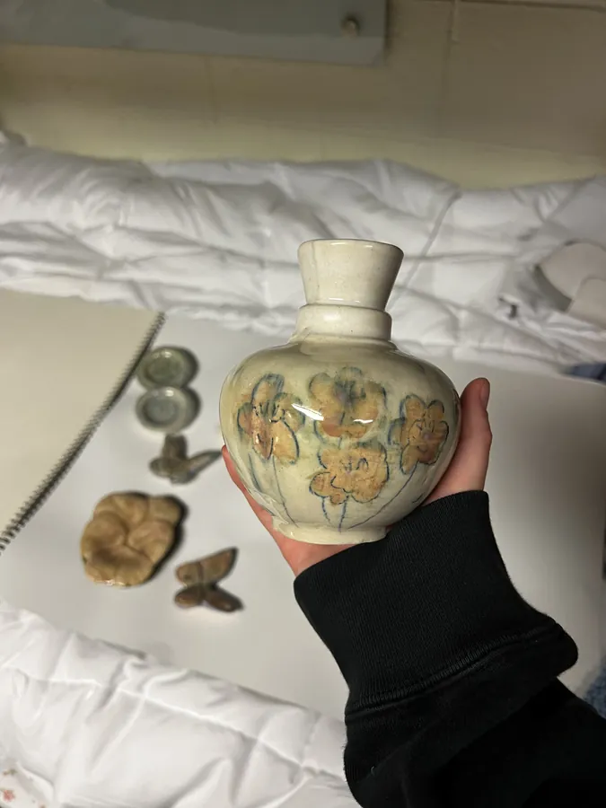 A hand-thrown ceramic vase painted with orange blossoms, held up to the camera.