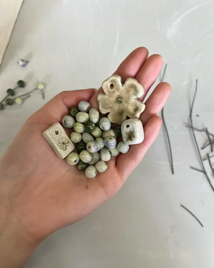 A handful of glass beads and handmade ceramic beads, held over a work surface.
