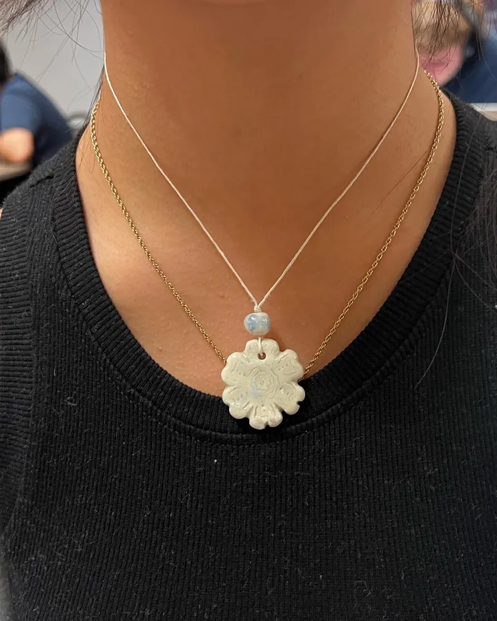 A necklace with a carved white ceramic flower pendant, worn.