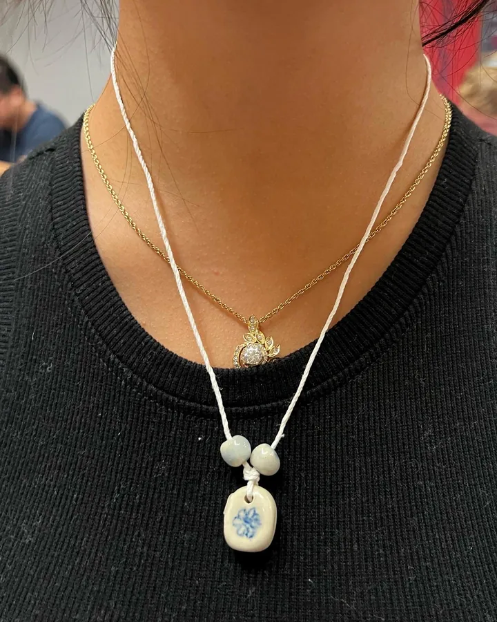 A necklace with a small blue and white painted ceramic pendant, worn.