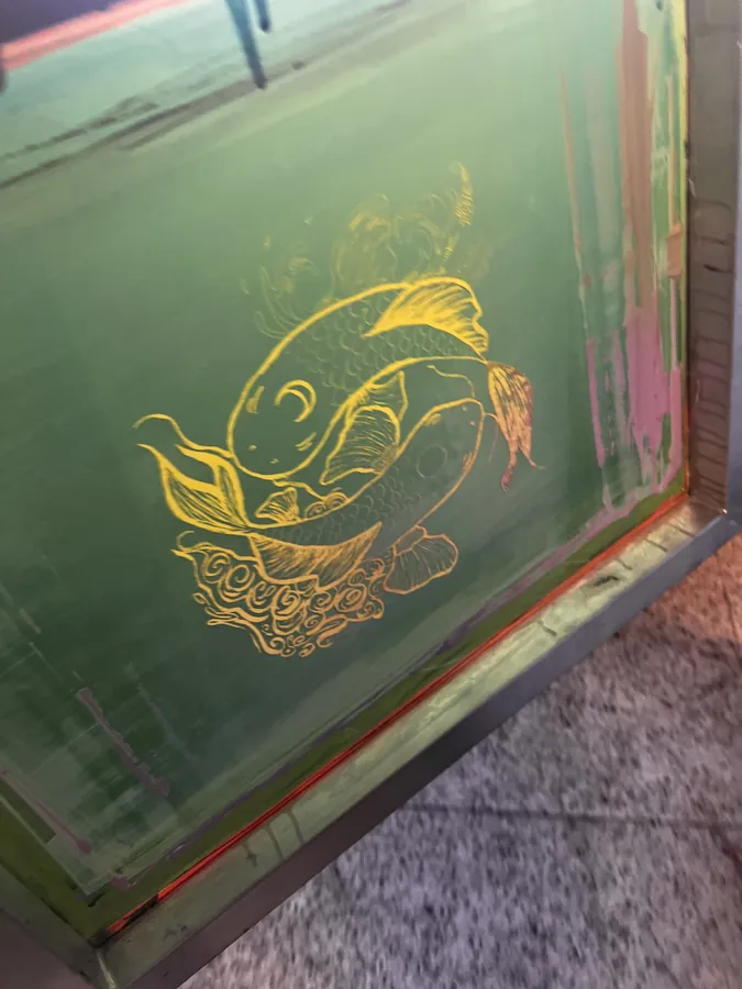 A screenprinting screen holding a koi fish design in yellow emulsion.