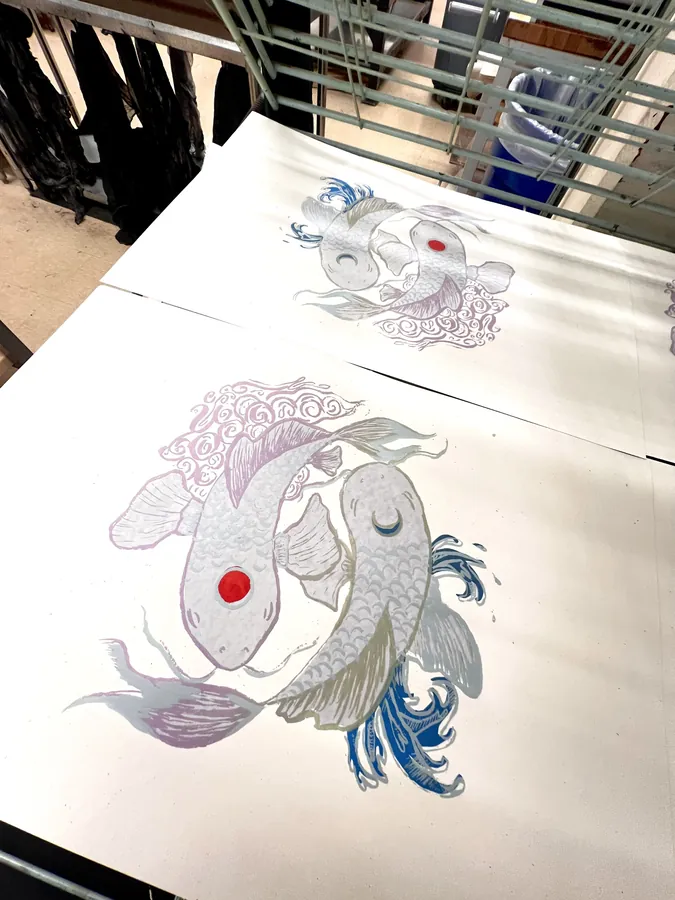 Finished screenprints of two koi fish in pink and blue, laid out on paper.
