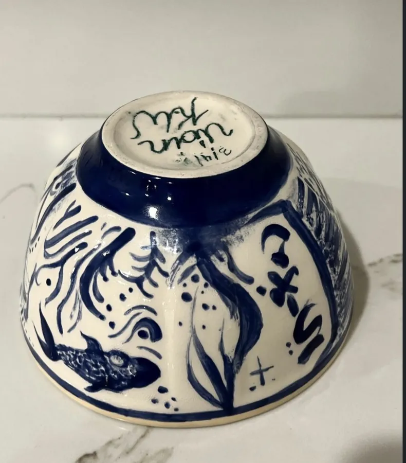 The underside of a blue and white ceramic bowl painted with fish and waves.