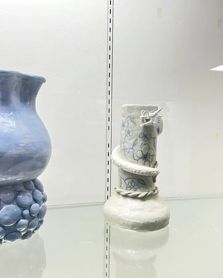 A ceramic dragon lamp on a white shelf, beside a blue glazed vase.