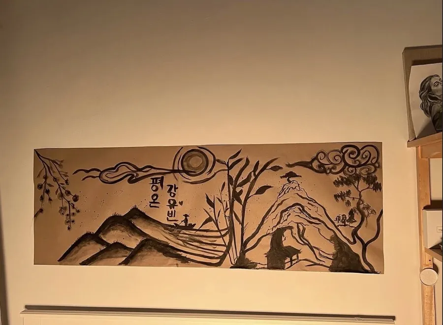 A long horizontal ink painting of mountains and a sun with Korean lettering, framed on a wall.