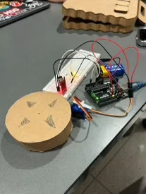 A laser-cut wooden puck with four arrows on its face, wired to an Arduino board on a workbench.